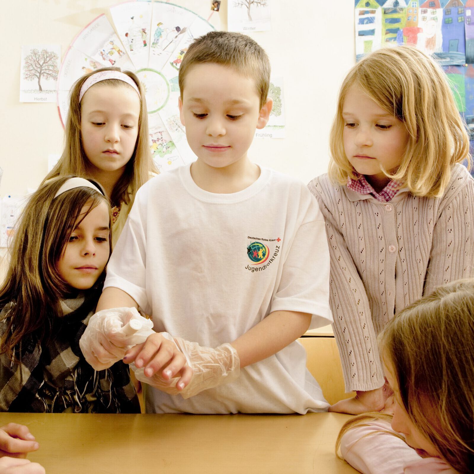Erste Hilfe in der Grundschule: Junge, der Mitglied beim Jugendrotkreuz ist, demonstriert Schülern Erste Hilfe